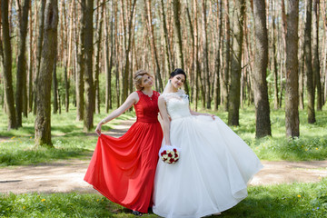 Bride with witness wearing red dress walking in forest