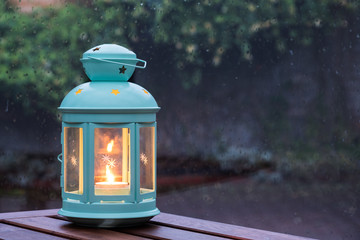 Scented candle in a pretty lantern with outdoor background in a rainy evening