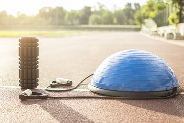 Close up of a bosu ball on a running track. Sport and fitness equipment. Foam roller for massage and pilates ball. Lens flare in the background.
