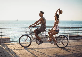 Tuinposter Portrait of a mixed race couple on tandem bicycle outdoors near the sea © sashafolly