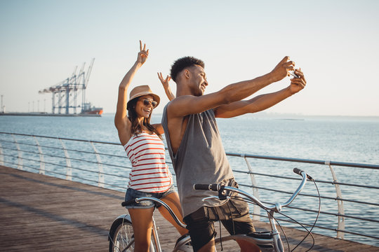 Portrait Of A Mixed Race Couple Doing Selfie On Tandem Bicycle Outdoors Near The Sea