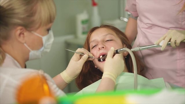 The orthodontist of the dental clinic does the oral cleaning, the young patient is waiting for the completion of the treatment, the nurse is holding the instrument in his hand