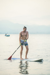 Young european man tourist practicing paddle boarding in sea at beach near ancient fortress wall and shipyard in city center of Alanya, Mediterranean Turkey