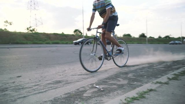 Young hipster man sliding on fixed gear bicycle in dust on the road, slow motion