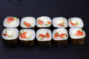 Delicious maki sushi roll with salmon,avocado and tofu cheese served on black slate, close up. Japanese food.