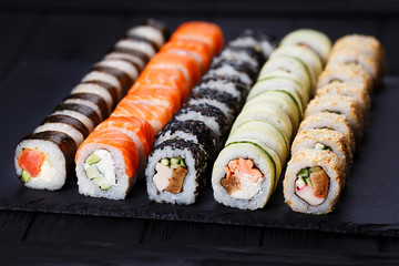 Japanese cuisine, restaurant menu photo of multicolored appetizing set of sushi served on  black slate, close up. © Vadym