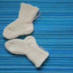 Вязаные белые детские носочки на бирюзовом фоне