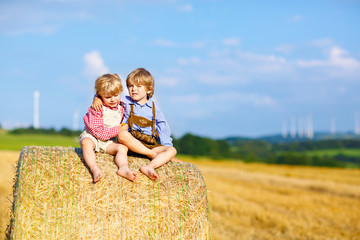 Naklejka na ściany i meble Two little kid boys, twins and siblings sitting on warm summer day on hay stack
