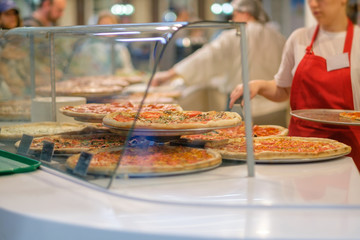 Variety of yummy pizzas under shopping window in pizzeria