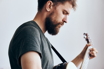 Young guy with a beard with on a light background playing a guitar