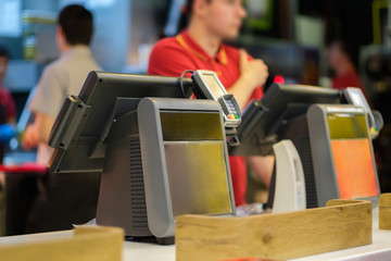 Cash and order desk with order screen and card payment terminal with cashiers on back  in fast food restaurant