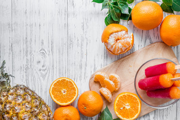 Obraz na płótnie Canvas Fresh oranges, mandarins, pineapple, ice cream on wooden background top view copyspace