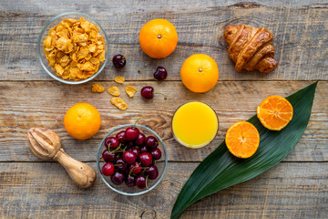 Light summer breakfast. Muesli, oranges, cherry and croissant on wooden table background top view