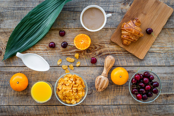 Light summer breakfast. Muesli, oranges, cherry, croissant and coffee on wooden table background top view