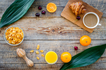 Light tasty breakfast. Muesli, oranges, cherry, french croissant, milky coffee on wooden background top view copyspace