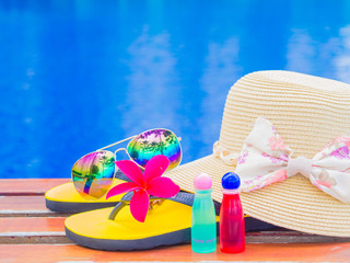 Sunglasses with summer hat, flip flops, shampoo, lotion  and flowers by the swimming pool. Vacation...