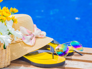 Sunglasses with summer hat, flip flops, shampoo, sunscreen lotion  and flowers by the swimming...