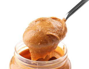 Creamy peanut butter in spoon and jar on white background