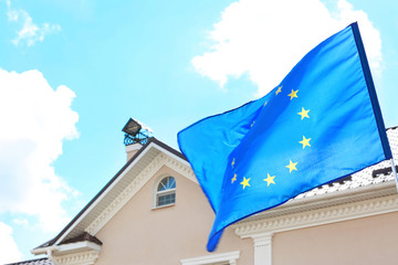Waving European flag and house roof with blue sky on background