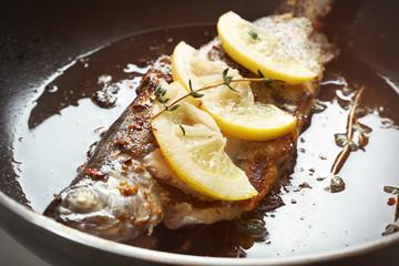 Frying pan with tasty trout fish and lemon slices, closeup