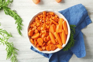 Slices of carrot in bowl on wooden background