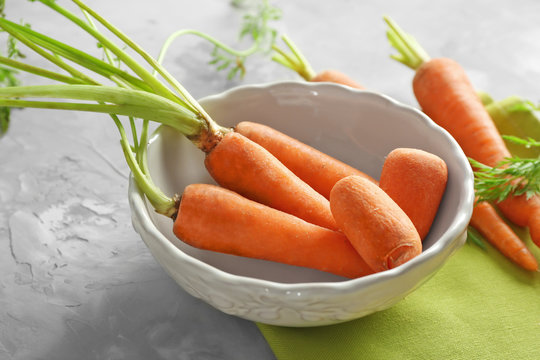 Bowl with fresh carrot on grey background