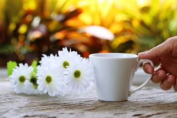 Hand drinking coffee in the morning closeup on wooden table with white daisy blur background