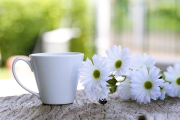 White coffee cup closeup on wooden table with white daisy blur background