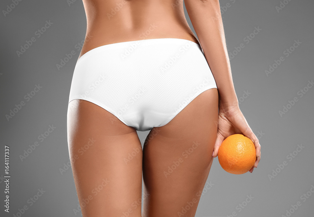 Sticker Young woman holding orange on grey background. Cellulite problem concept