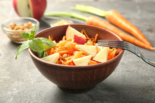Fototapeta Delicious carrot raisin salad with apple in brown clay bowl on table