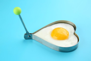 Fried sunny side up egg in heart shaped mold on color background