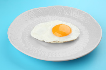 Plate with delicious sunny side up egg on color background