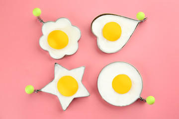 Fried sunny side up eggs in molds of different shapes on color background
