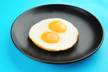 Plate with delicious sunny side up eggs on color background
