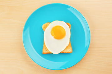 Plate with delicious sunny side up egg and toast on wooden background