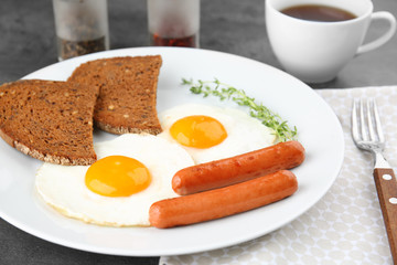 Plate of over easy fried eggs with sausages, bread and cup of tea on table