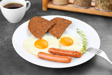 Plate of over easy fried eggs with sausages, bread and cup of tea on table