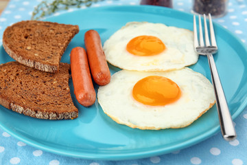 Homemade over easy fried eggs with sausages and bread on plate
