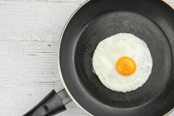 Frying pan with tasty over easy egg on wooden table
