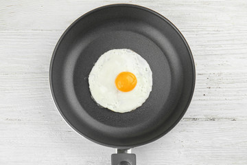 Frying pan with tasty over easy egg on wooden table