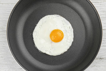 Frying pan with tasty over easy egg on wooden table