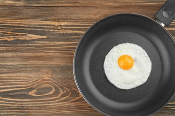 Tasty over easy fried egg in pan on wooden table