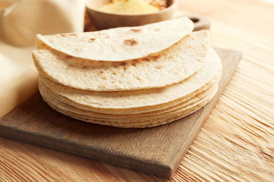 Board with stack of yummy tortillas on wooden table