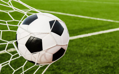 Naklejka na ściany i meble Soccer football in Goal net with green grass field.
