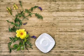 flat lay of yellow rose and wild flowers with empty white saucer on a wooden table with copy space for your text