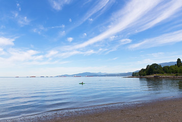 Sea landscape at the city beach in Vancouver, Canada. Kayaking in the sea with ships in the roadstead and snow mountains on horizon.