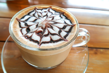A cup of latte art on the glass saucer on the wood table