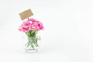 Pink carnation flowers bouquet in glass with blank brown note on white background with copy space