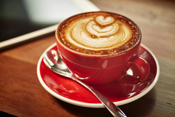 Red cup of cappuccino with beautiful latte art on old wooden background