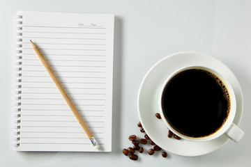 White cup of coffee morning on wooden table with notebook